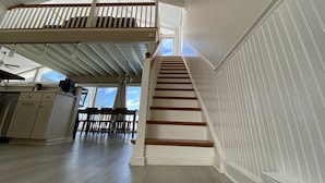 Eine geräumige Küche mit hohen Decken, einer Treppe mit weißen Geländern und einem Essbereich mit Stühlen.