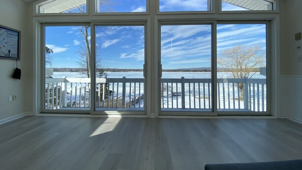 Ein geräumiges Zimmer mit großen Fenstern und Blick auf einen zugefrorenen See sowie einen weißen Zaun.