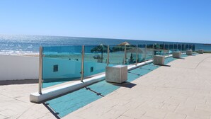 Un área de piscina en la azotea con agua azul cristalina, barandilla de vidrio y vista al océano.