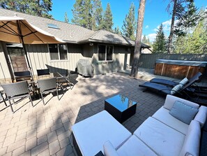 A backyard patio with a covered grill, outdoor seating, and a hot tub.