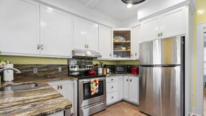 A modern kitchen with white cabinets, stainless steel appliances, and a granite countertop. - Walk to Downtown Brevard  Pets Welcome Large Fenced Yard Porches Biking Hiking (Brevard)