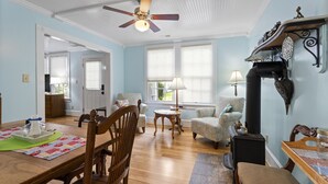 A spacious living room with a wooden dining table, two armchairs, a sofa, a fireplace, and a ceiling fan. - Walk to Downtown Brevard  Pets Welcome Large Fenced Yard Porches Biking Hiking (Brevard)