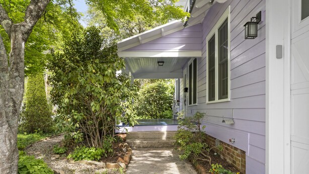 A house with a covered porch, a brick foundation, and a garden with various plants and a pathway leading to the entrance. - Walk to Downtown Brevard  Pets Welcome Large Fenced Yard Porches Biking Hiking (Brevard)