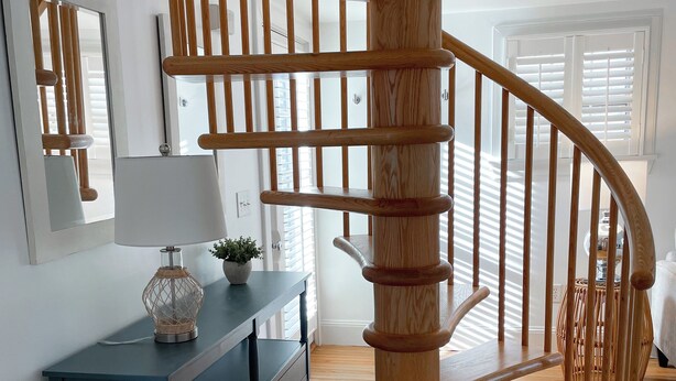 Una escalera en espiral de madera en una habitación con un aparador azul oscuro, una lámpara y una planta en maceta.