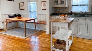 Una cocina moderna con armarios blancos, una mesa de comedor de madera y un banco empotrado con un cojín de colores.