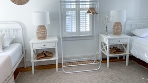 Un dormitorio con cama, dos mesitas de noche, una ventana con persianas, una lámpara colgante y un radiador blanco.