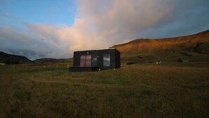 A modern, minimalist house in a grassy field with rolling hills in the background.