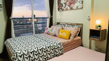 A bedroom with a bed, a view of the cityscape, a painting, and a bedside lamp.
