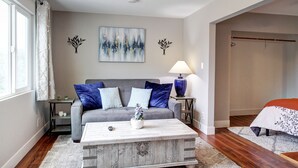 Ein Wohnzimmer mit grauem Sofa, blauen Kissen, einem weißen Couchtisch und einem Bild an der Wand.