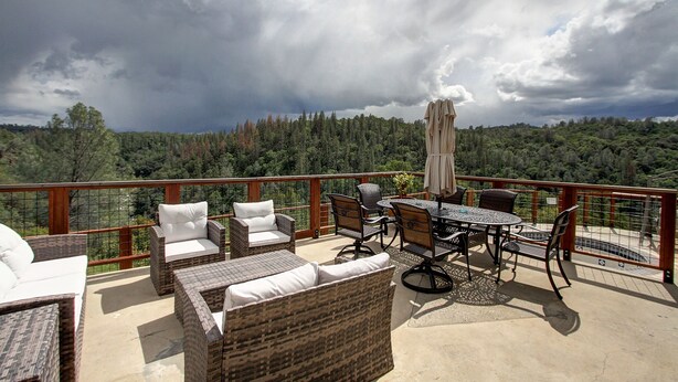 Eine Terrasse mit Korbmöbeln, einem Tisch und Stühlen, mit Blick auf ein bewaldetes Gebiet.