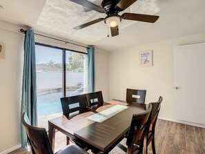 Un coin repas comprenant une table et des chaises, un ventilateur de plafond, une fenêtre avec des rideaux et une porte.