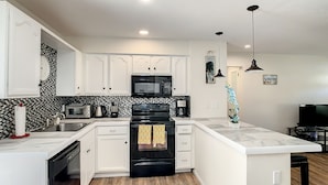 A modern kitchen with white cabinetry, a black stove, a microwave, and a coffee maker.