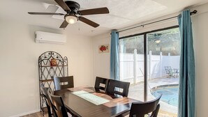 A dining area with a table, chairs, a ceiling fan, and a view of a swimming pool through a glass door.