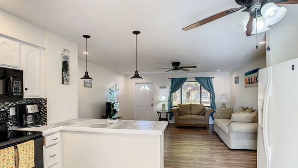 A modern kitchen with a central island, a dining area with a sofa, and a ceiling fan.