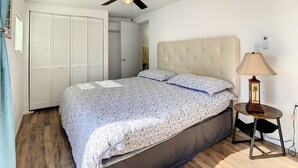 A bedroom with a bed, a ceiling fan, a bedside table with a lamp, and a wardrobe.