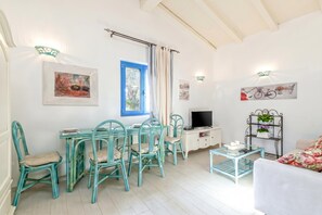 Une pièce comprenant une table à manger et des chaises, un téléviseur, une bibliothèque et une fenêtre avec des rideaux.