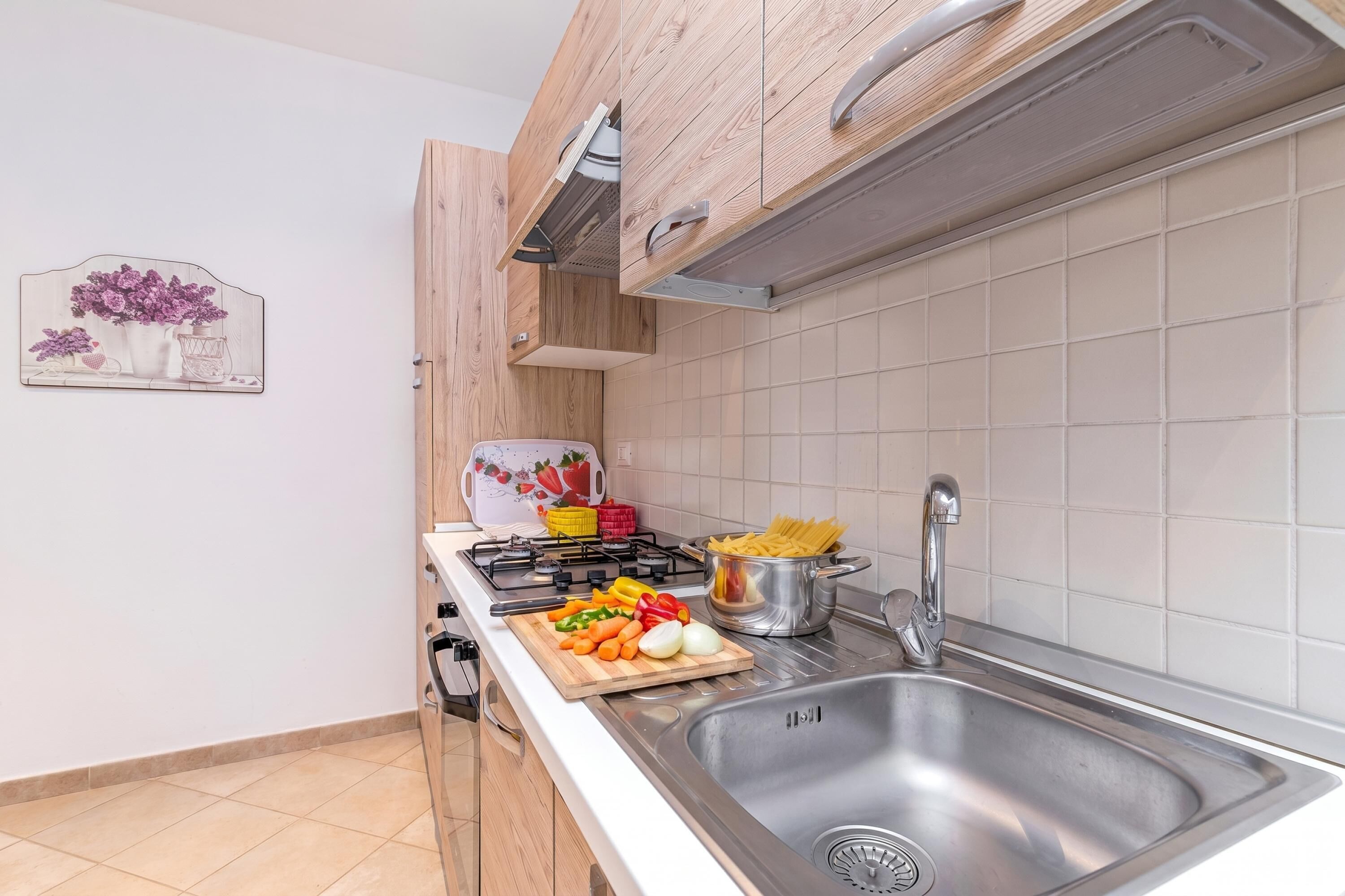 Une cuisine équipée d’un évier en acier inoxydable, d’une cuisinière à gaz et d’une planche à découper avec des légumes.