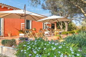 A patio with outdoor seating, a red building, and a garden with flowers.