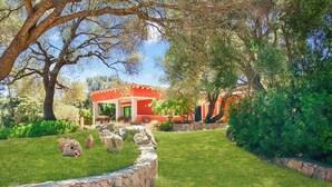A garden with a stone wall, a red building, and trees.
