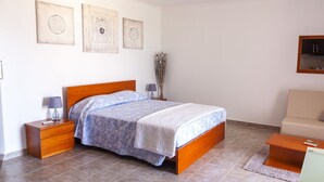 A bedroom with a wooden bed, two bedside tables with lamps, a nightstand, a vase with dried flowers, and a framed picture on the wall.