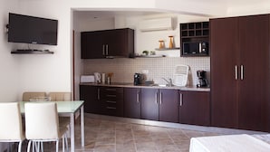 A modern kitchen with dark cabinets, a tiled backsplash, a flat-screen TV, a coffee machine, and a dining area with a table and chairs.