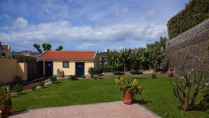 A courtyard with a tiled floor, a yellow building with a red roof, and various potted plants.