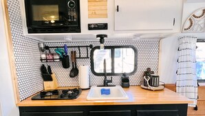 A compact kitchen with a microwave, stove, sink, and storage cabinets. - Cute Renovated RV Near Zion & St. George (Leeds)