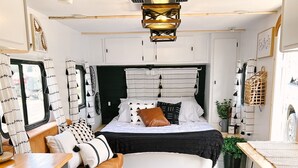 A compact, modern room with a bed, wooden flooring, a black rug, and a kitchen area with a counter and cabinets. - Cute Renovated RV Near Zion & St. George (Leeds)