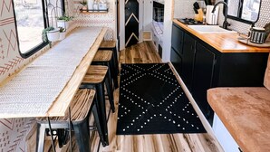 A compact RV kitchen with a wooden table, bar stools, a black rug, and a small dining area. - Cute Renovated RV Near Zion & St. George (Leeds)