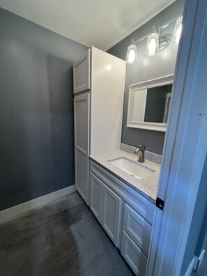 Et badeværelse med et hvidt toiletbord, vask, spejl og en lysarmatur over spejlet.