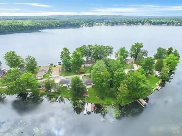 En ejendom ved søen med en anløbsbro, omgivet af frodig vegetation og boliger.