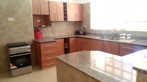 A kitchen with wooden cabinets, a granite countertop, and a gas stove. - TIGONI GEM GARDENS (Limuru)