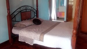 A bedroom with a wooden four-poster bed, a herringbone-patterned floor, and a view of a room with a mirror and curtains. - TIGONI GEM GARDENS (Limuru)