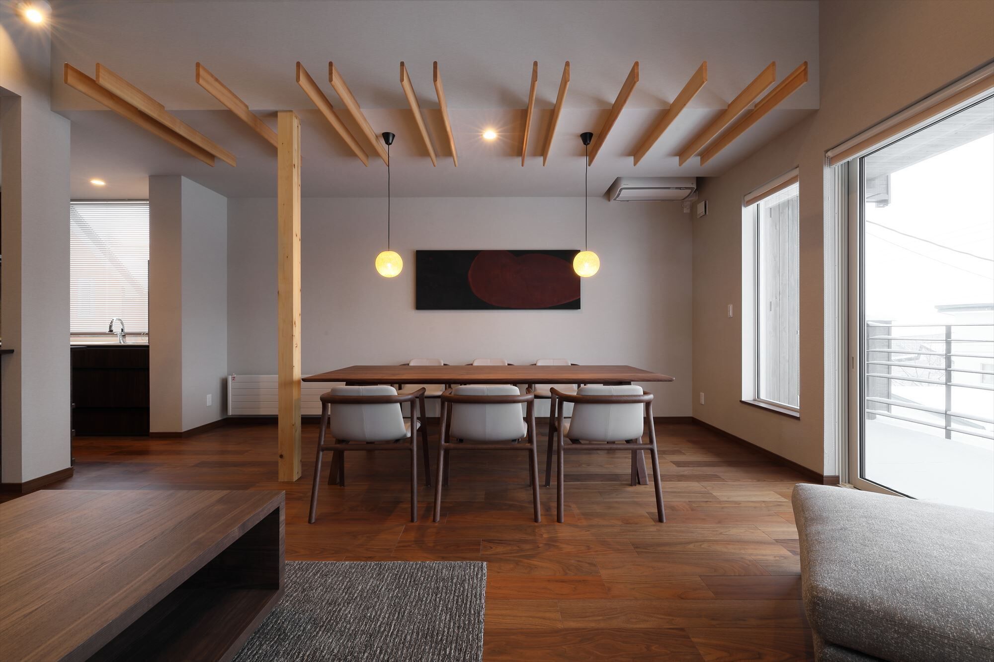 A modern dining area with a wooden table and chairs, a large abstract painting, and a view of the outdoors.