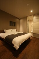 A modern hotel room with a large bed, a wooden floor, a sliding door closet, and a small bedside table.