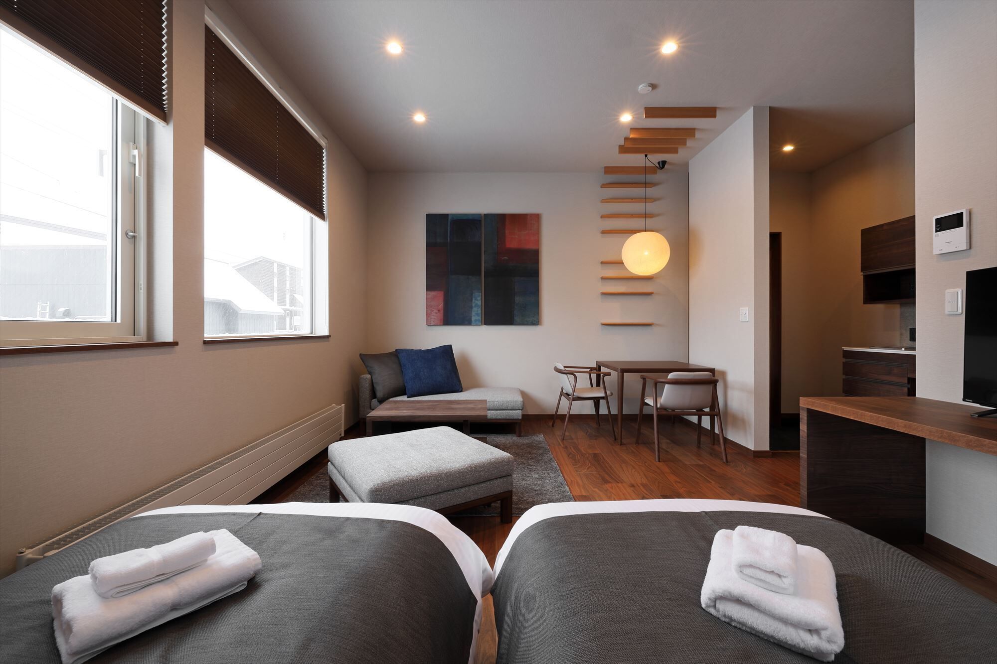 A hotel room with two beds, a sofa, a dining table, and a TV.