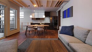 A modern living room with a wooden dining table, two chairs, a sofa, and a kitchen in the background. - Orchid Furano (Furano)