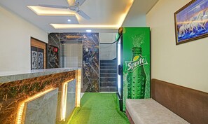 A modern lobby with a marble reception desk, a green Sprite advertisement, a ceiling fan, and a framed artwork on the wall. - Treebo Jayshree Palace C21 Business Park (Indore)