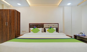 A hotel room with a wooden wardrobe, a bed with a green and purple bedspread, and a nightstand with a water bottle and a cup. - Treebo Jayshree Palace C21 Business Park (Indore)