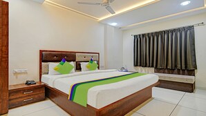 A neatly arranged bedroom with a wooden headboard, a bed with a colorful bedspread, a bedside table with a phone, and a window with curtains.
