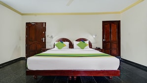 A hotel room with a bed, two wooden doors, a nightstand, and a wall-mounted light. - Itsy Hotels The Waters Edge Beach Resort (Neyyattinkara)