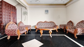 A room with a wooden cabinet, patterned sofas, a round wooden table, and a black tiled floor. - Itsy Hotels The Waters Edge Beach Resort (Neyyattinkara)