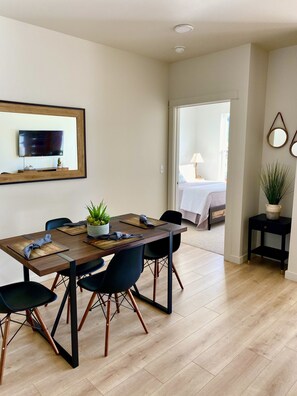 A dining area with a wooden table, black chairs, and a potted plant. A television is mounted on the wall above the table.
