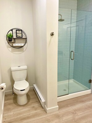 A bathroom with a toilet, a glass shower enclosure, and a wall-mounted shelf with a plant and a motivational quote. - Paradise Valley View Getaway (Livingston)