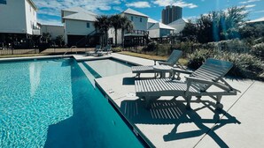 A swimming pool with lounge chairs, surrounded by residential buildings and palm trees. - Excellent Location, Beautiful House Sleeps 10 and Will Feel Like Home!  (Orange Beach)