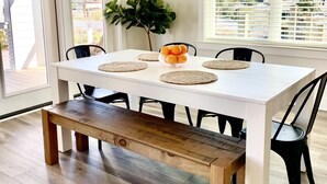 A dining area with a white table, black chairs, a wooden bench, a plant, and a view of the city through large windows. - Excellent Location, Beautiful House Sleeps 10 and Will Feel Like Home!  (Orange Beach)