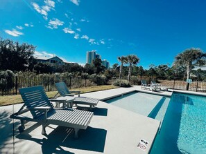 A swimming pool with lounge chairs and a picnic table, surrounded by a fence and trees.