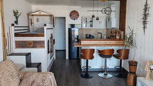 Un espacio habitable compacto con kitchenette, una zona de comedor con taburetes de bar y un rincón de estar acogedor con sofá y manta.