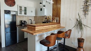 Una cocina moderna con una isla de madera, taburetes de bar, un refrigerador negro y un reloj en la pared.