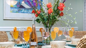 Uma mesa de jantar posta com copos de vidro, uma garrafa de vinho e um vaso com flores.
